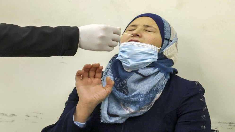 عامل صحي يجمع عينة مسحة أنف من امرأة فلسطينية لاختبار فيروس كورونا COVID-19 في قرية دورا غربي الخليل ، في الضفة الغربية المحتلة .1 يناير 2022.(أ ف ب)