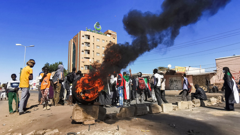 متظاهرون بجوار إطار مشتعل عند حاجز مؤقت أقيم أثناء احتجاج للمطالبة بالحكم المدني في "شارع 40" في العاصمة السودانية أم درمان. 4 يناير/ كانون الثاني 2022. (أ ف ب)