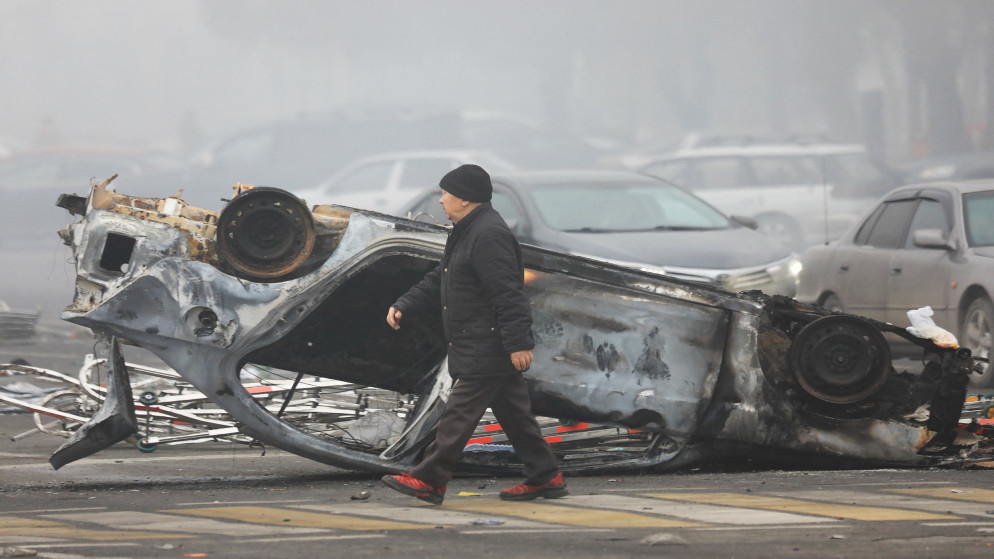 رجل يسير بقرب مركبة محترقة في ألماتي في كازاخستان. (أ ف ب)
