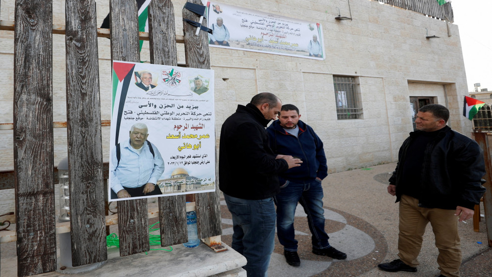 فلسطينيون يقفون بجوار ملصق للشهيد عمر عبد المجيد أسعد (80 عامًا)، في قرية جلجليا شمال رام الله بالضفة الغربية المحتلة، 12 يناير/كانون الثاني 2022. (رويترز)