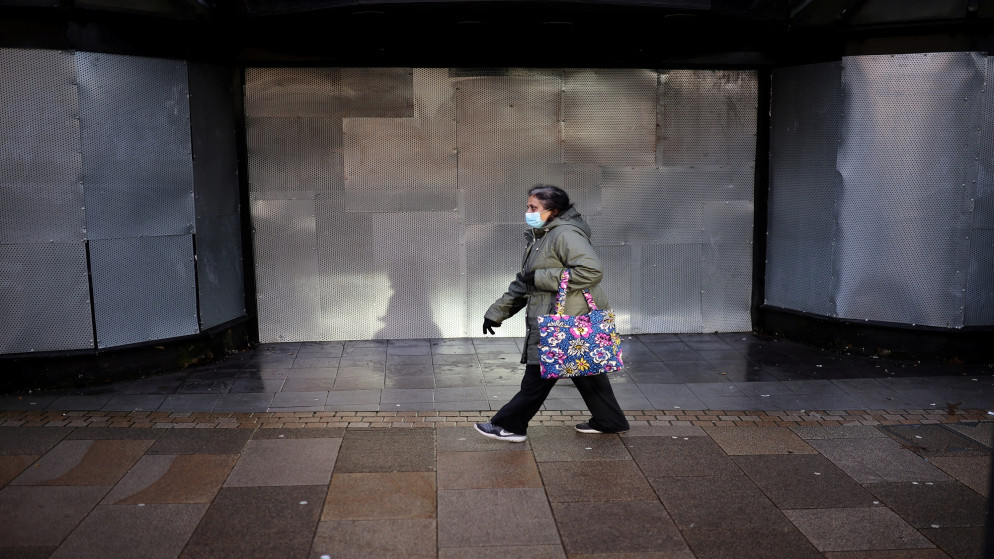 سيدة ترتدي كمامة للوقاية من فيروس كورونا المستجد تمشي أمام متجر مغلق في بريستون ببريطانيا. 11/01/2022. (فيل نوبل/ رويترز)