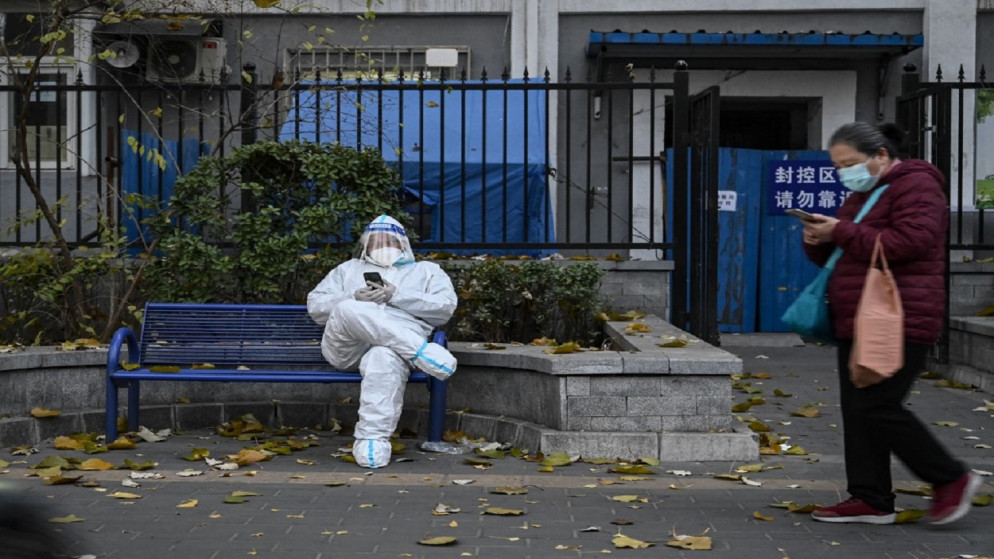رجل يرتدي معدات الحماية الشخصية (PPE) أثناء جلوسه خارج مبنى سكني مغلق بسبب قيود فيروس كورونا، في بكين، 22 نوفمبر 2022. (أ ف ب)