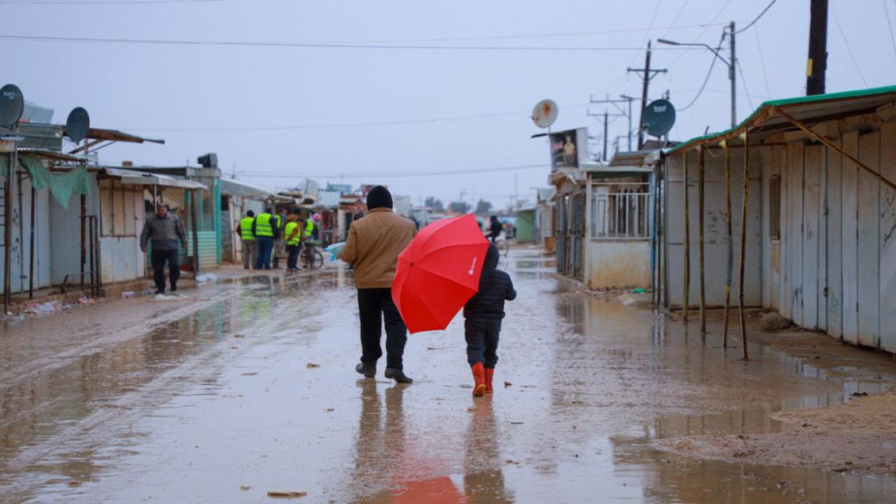 طفل سوري يحمل مظلة للوقاية من المطر يسير مع والده في أحد شوارع مخيم الزعتري بمحافظة المفرق. (مفوضية الأمم المتحدة للاجئين)