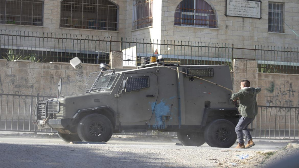 صورة أرشيفية لفلسطيني يلقي حجرا على مركبة تابعة لجيش الاحتلال الإسرائيلي في جنين. (وفا)