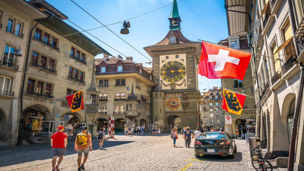 شارع قديم مع أعلام السياح وبرج الساعة في مدينة برن القديمة في سويسرا. (shutterstock)