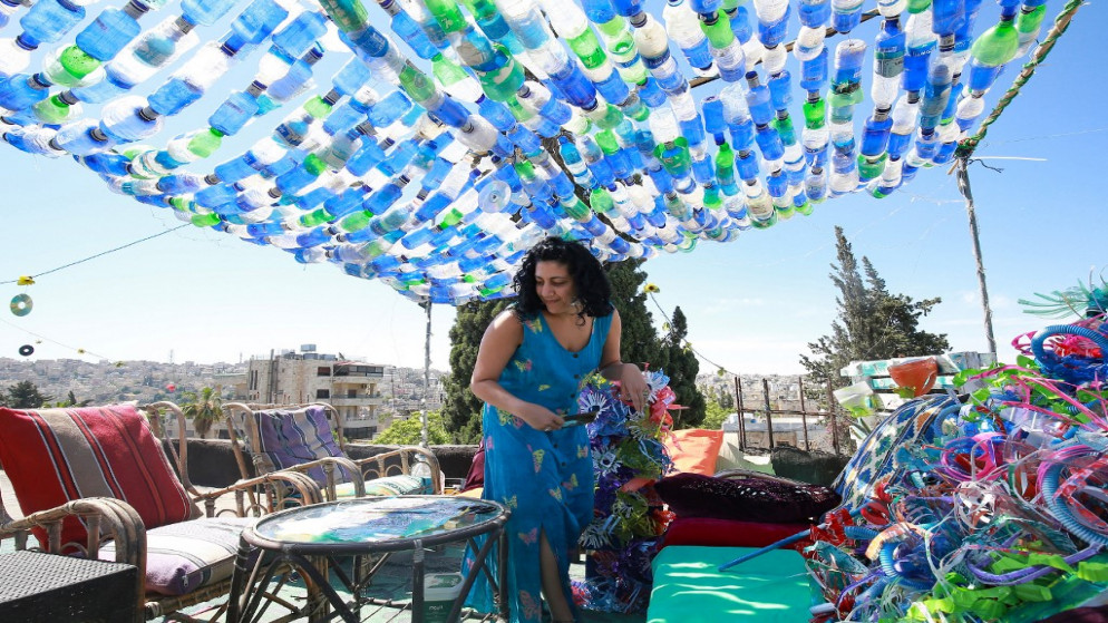 الفنانة ماريا نيسان على سطح مبنى منزلها تحت مظلة كبيرة من القناني البلاستيكية الملونة. (أ ف ب)