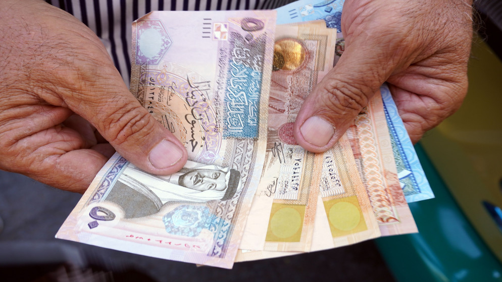 رجل يحمل بيده فئات من العملة الأردنية. (Shutterstock)