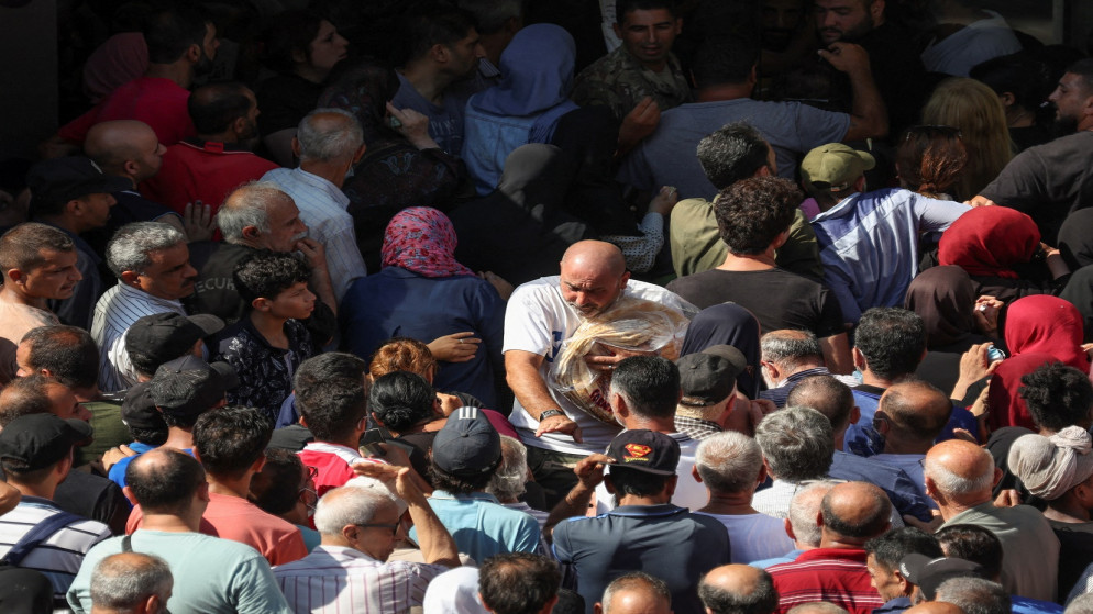 رجل يحمل أكواما من الخبز وهو يشق طريقه وسط حشد من الناس يصطفون في طابور للحصول على الخبز خارج مخبز في بيروت، لبنان، 27 تموز/يوليو 2022. (رويترز)