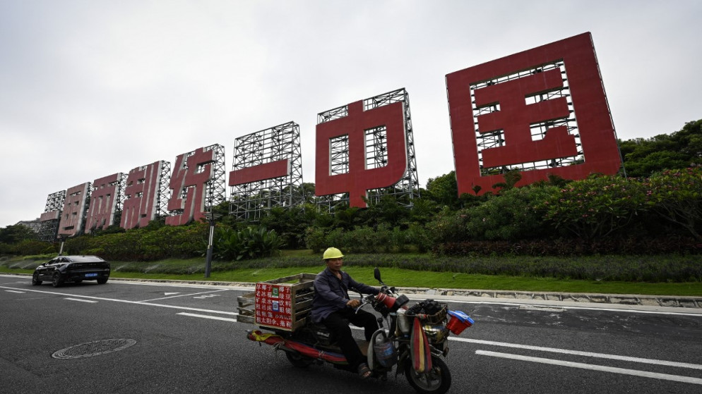 رجل يقود دراجة أمام لافتة ضخمة كُتب عليها "دولة واحدة ونظامان، ووحدة الصين" في شيامن بمقاطعة فوجيان جنوبي الصين. 25/07/2022. (جايد غاو / أ ف ب)