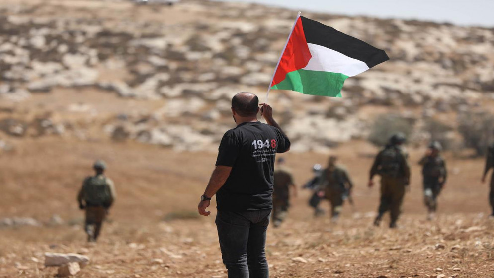 رجل يحمل العلم الفلسطيني خلال اعتداء قوات الاحتلال الإسرائيلي على مسافر يطا في الضفة الغربية المحتلة. (وفا)