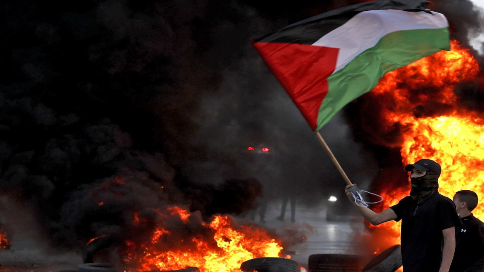 فلسطيني ملثم يلوح بالعلم الفلسطيني خلال مواجهات مع قوات الاحتلال الإسرائيلي بعد مسيرة الأعلام، 29 أيار/مايو 2022. (أ ف ب)