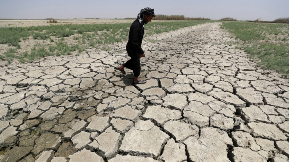رجل يمشي على تربة متصدعة وجافة في هور الحويزة بالقرب من مدينة العمارة جنوبي العراق. 27/07/2022. (أحمد الربيعي / أ ف ب)